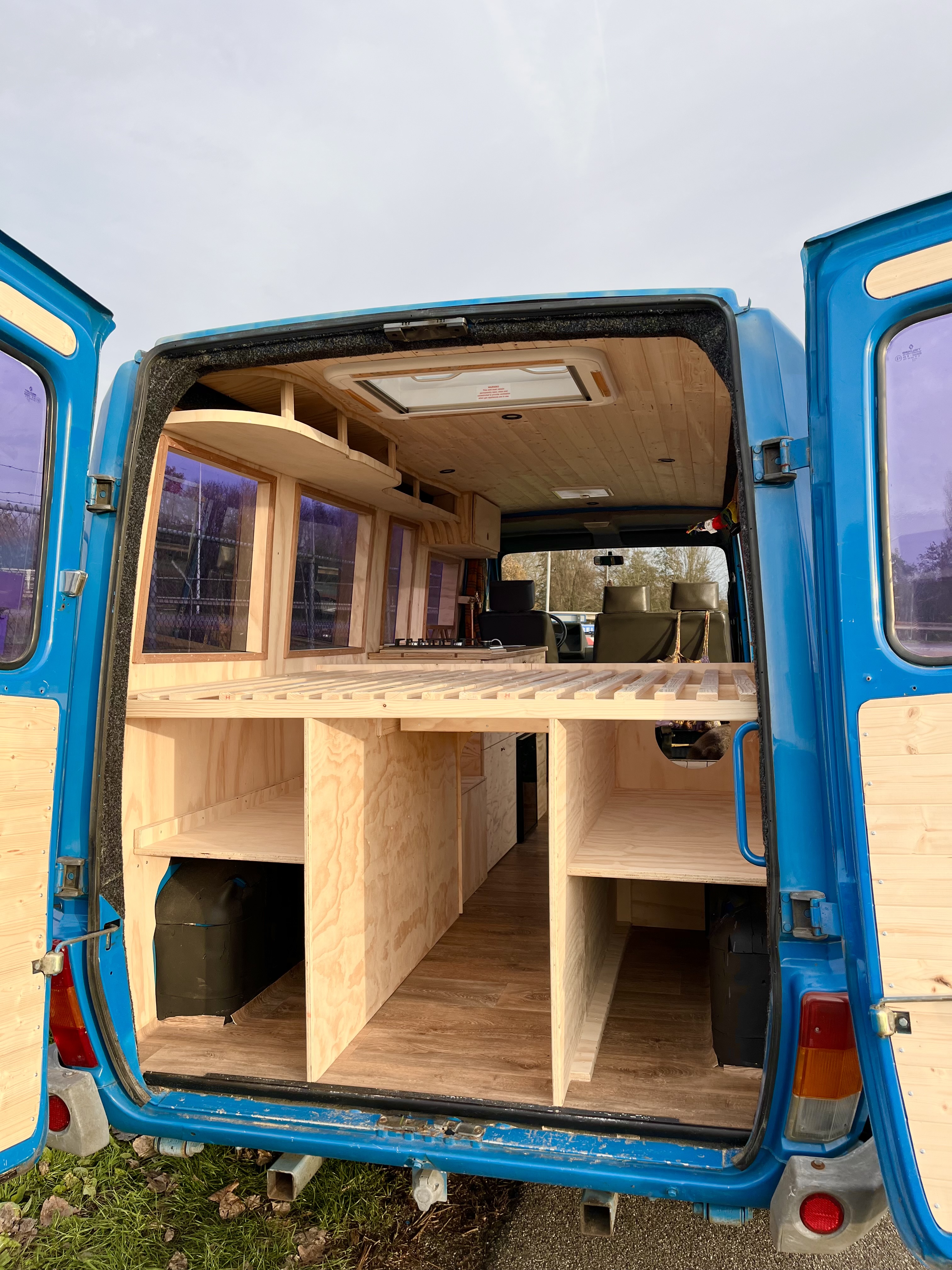 Blauwe bus open achterdeur: interieur in opbouwfase met bedframe en opbergvakken