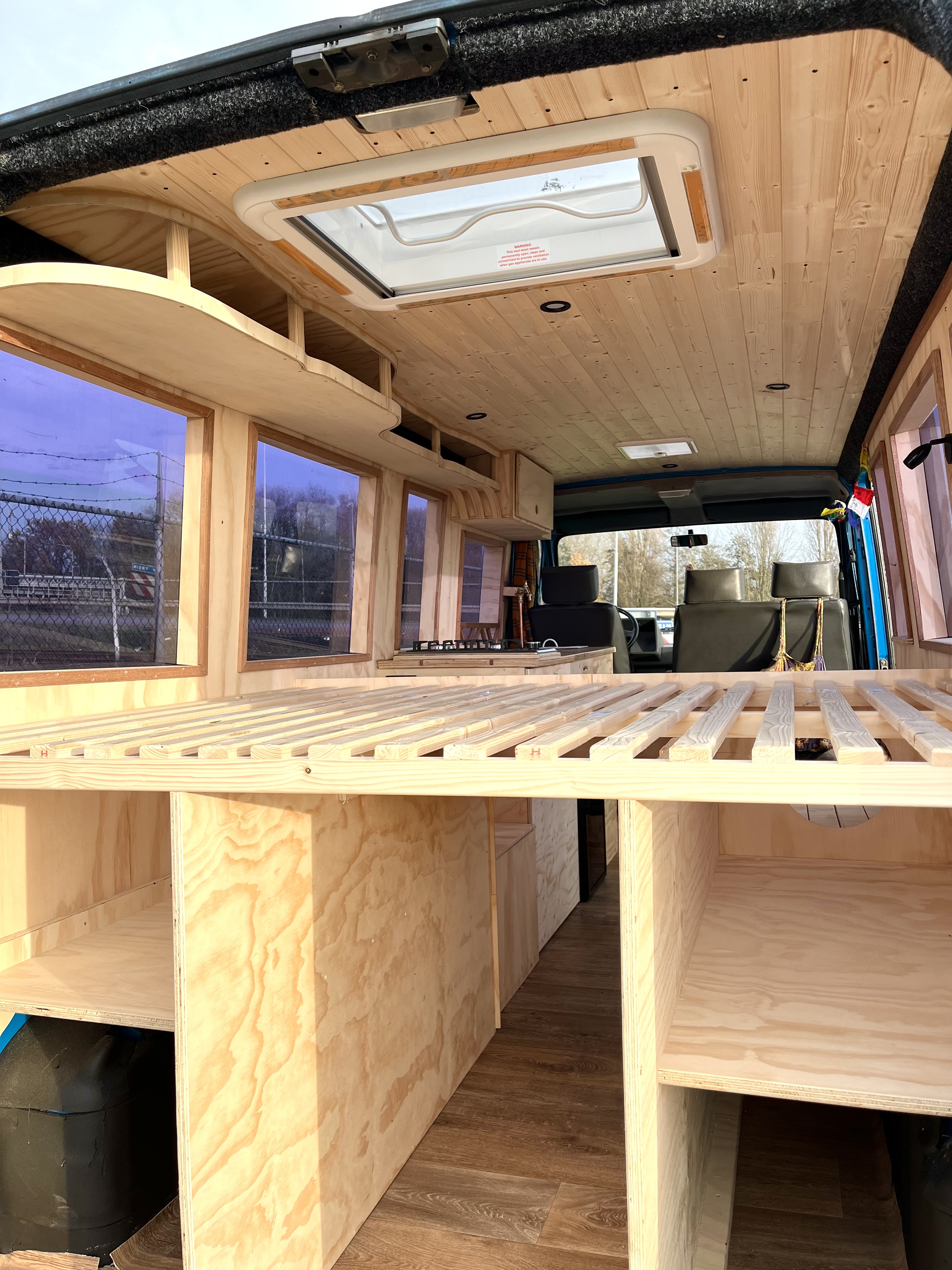 Blauwe bus interieur in opbouwfase: bedframe met latten, hangplanken en grenen plafond