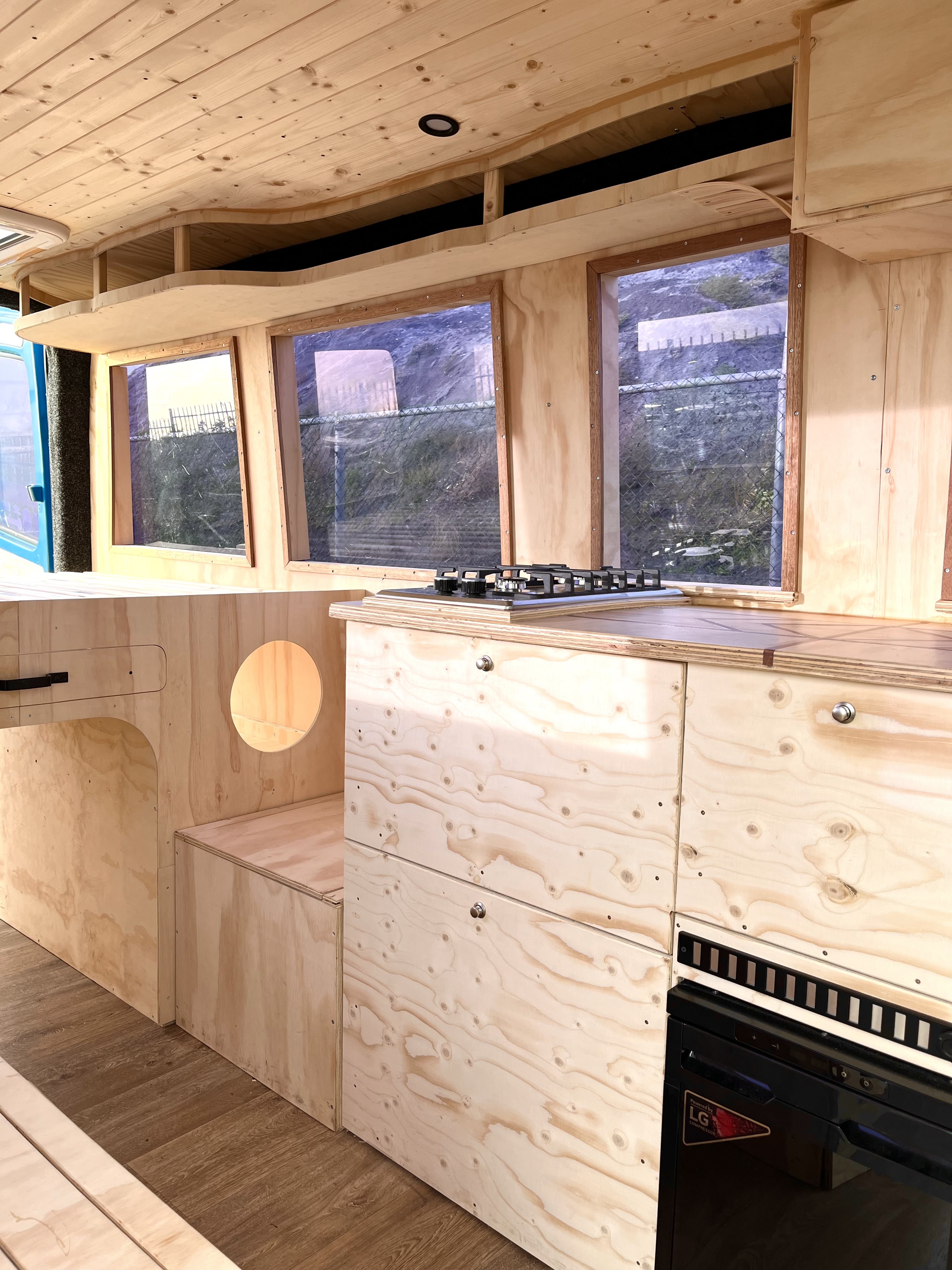 Blauwe bus keuken in opbouwfase: gasstel, kasten en drie ramen op de zijwand