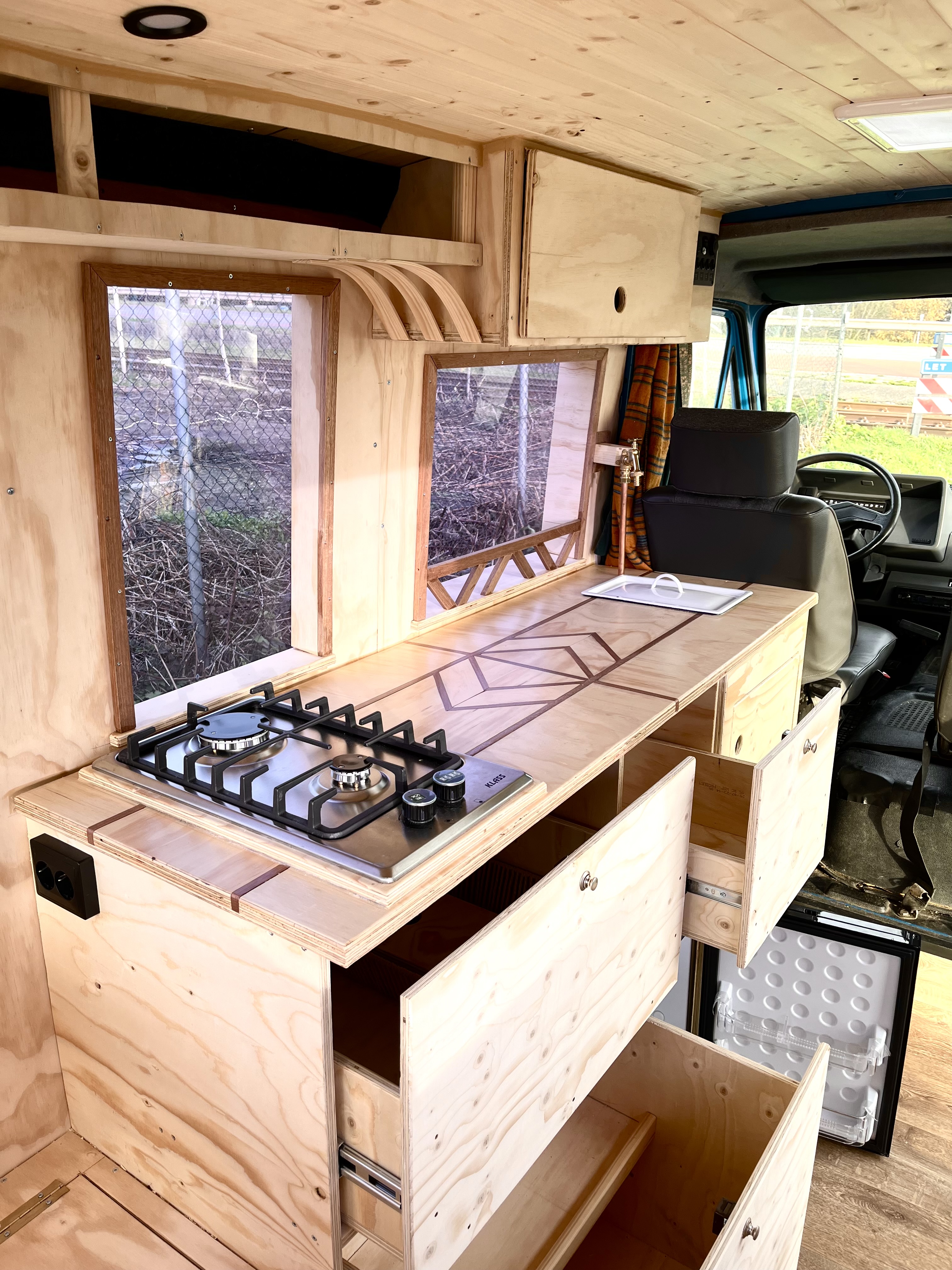 Blauwe bus keuken met ingebouwd gasstel, open lade en werkblad met ingefreesd patroon