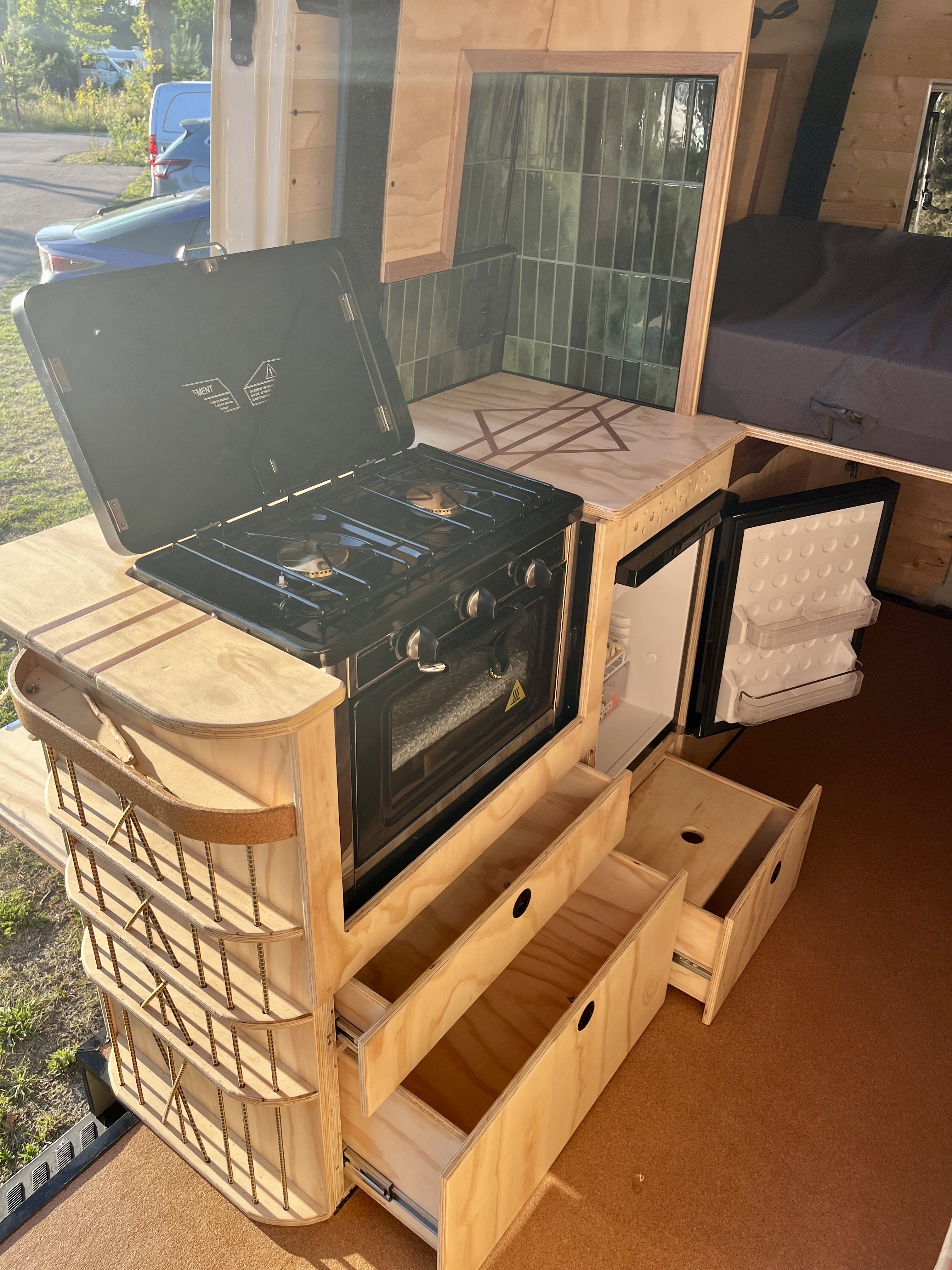 Uitgeklapte buitenkeuken met gasstel, oven en geopende koelkast bij zonsondergang