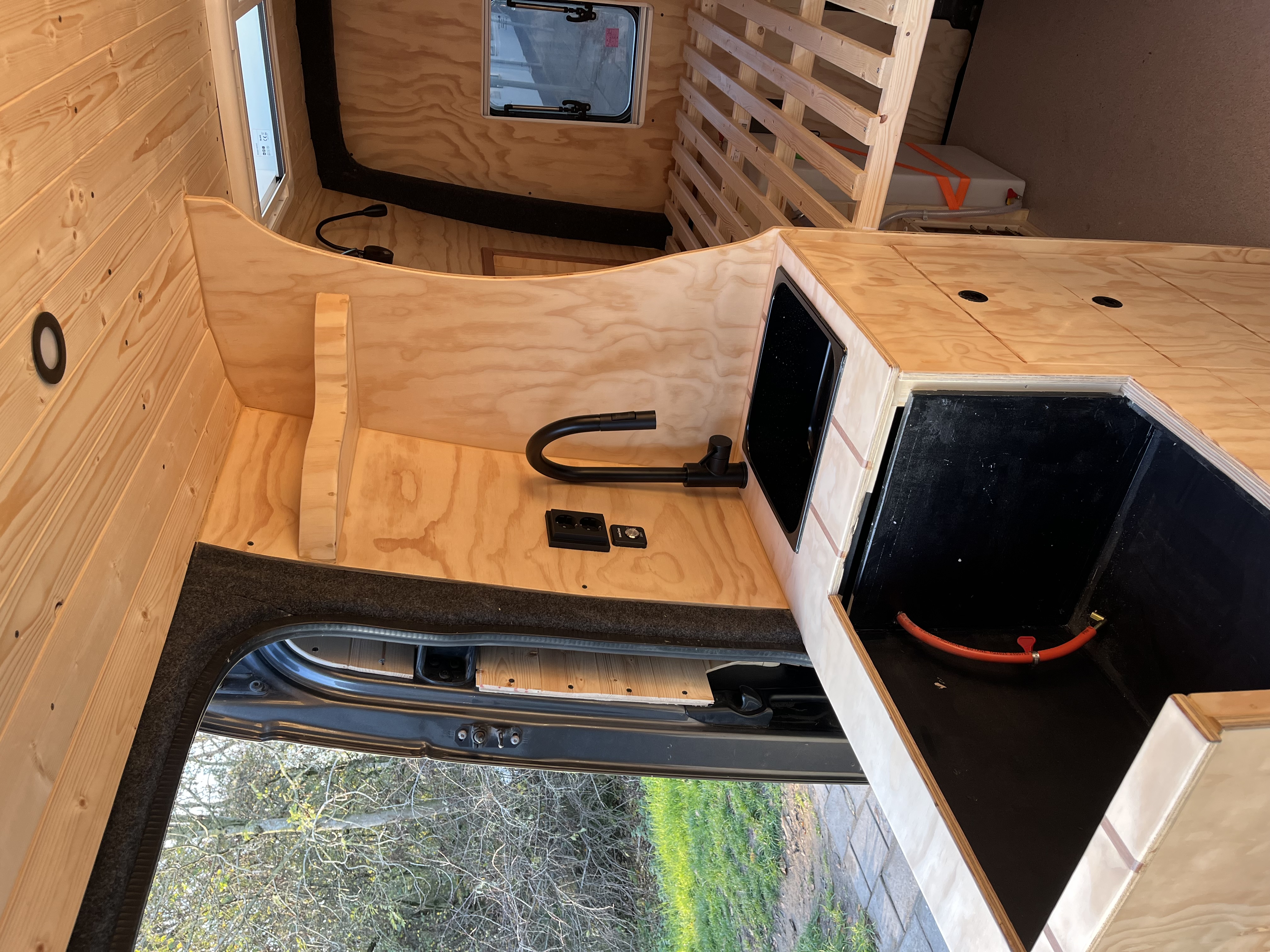 Keukenhoek met zwarte kraan en spoelbak, bedframe in aanbouw zichtbaar rechts