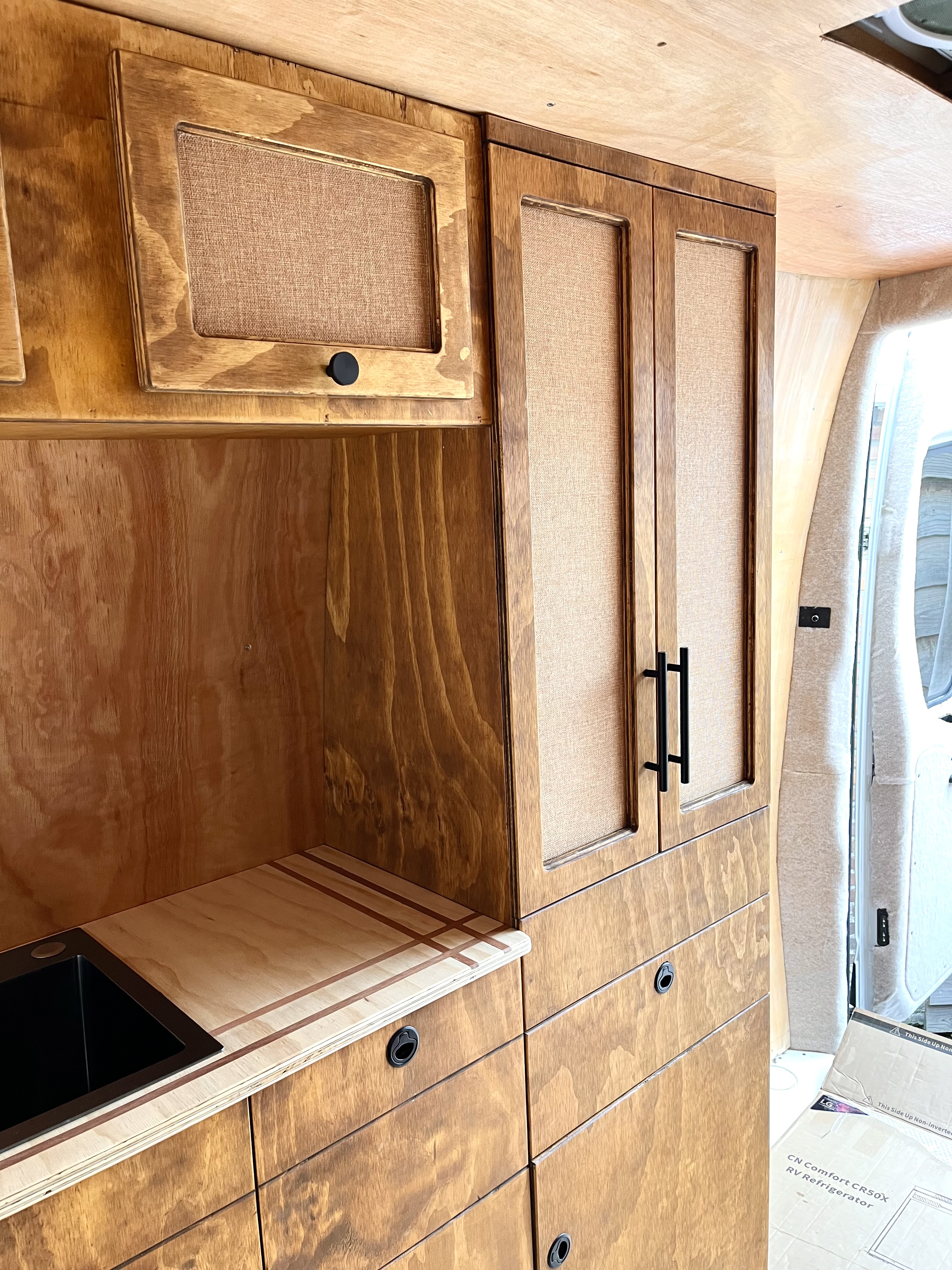 Detailopname keuken: donker gebeitste hangkasten met jute panelen en ingebouwde spoelbak